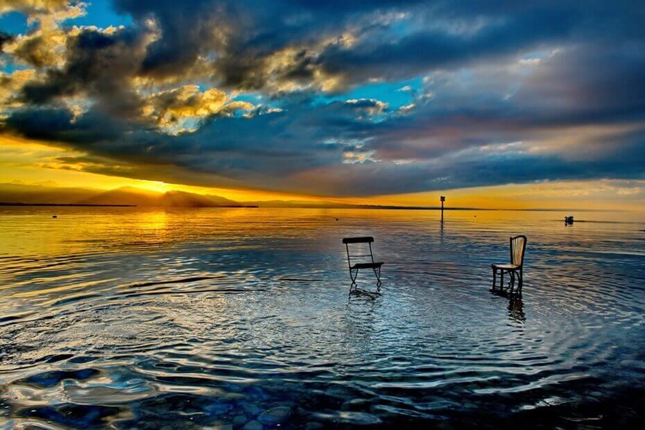 Nahe dem Ufer am Bodensee stehen zwei ungleiche Stühle im Wasser. Offenbar bedürfen die Stühle eine: zur Mediation.